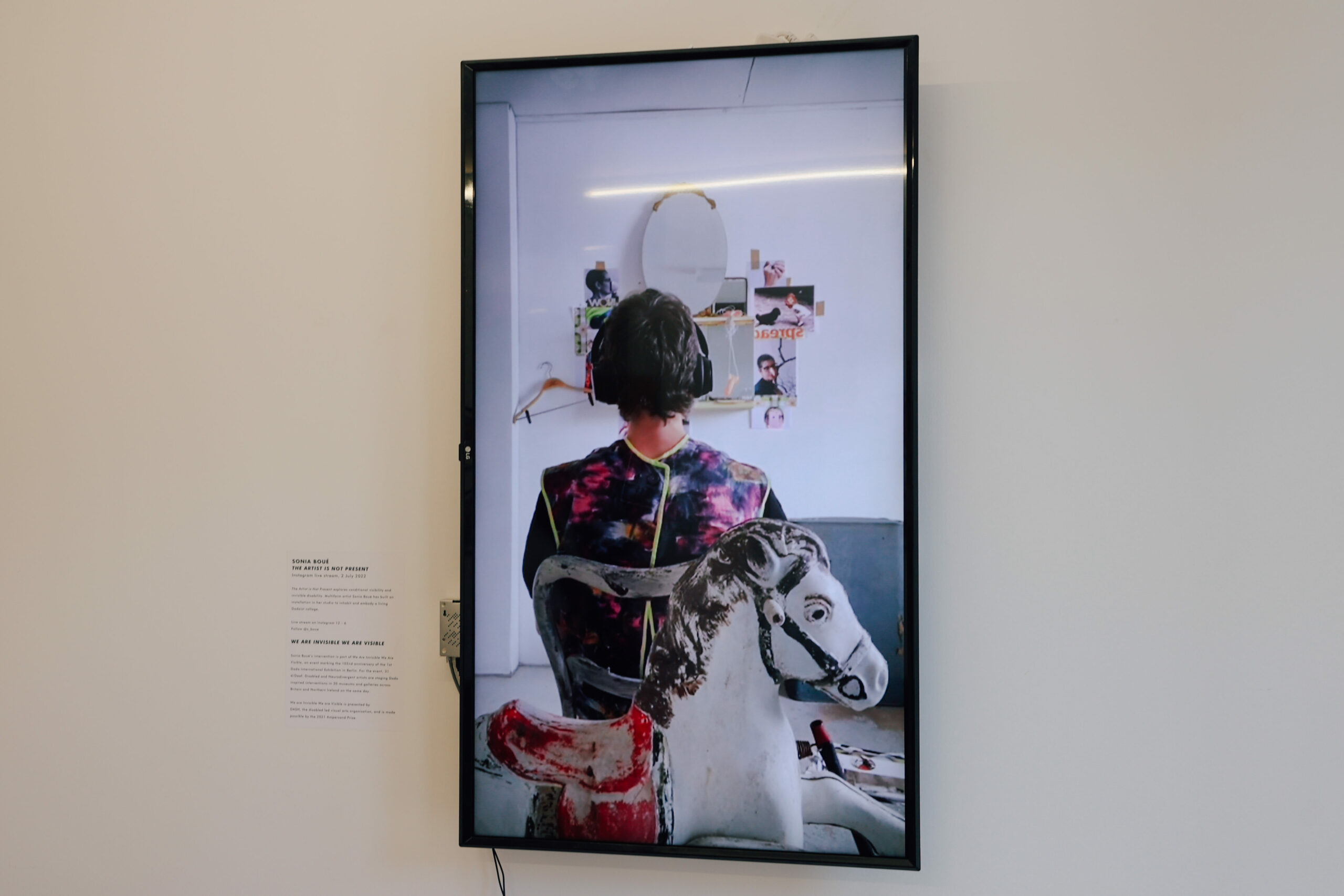 A screen in an exhibition showing an image of a seated person's back and a rocking horse.